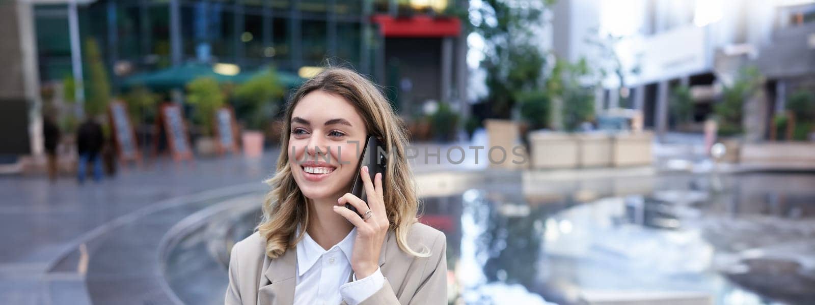 Vertical shot of smiling woman talking on mobile phone while sitting outside. Office lady waiting for someone after work.