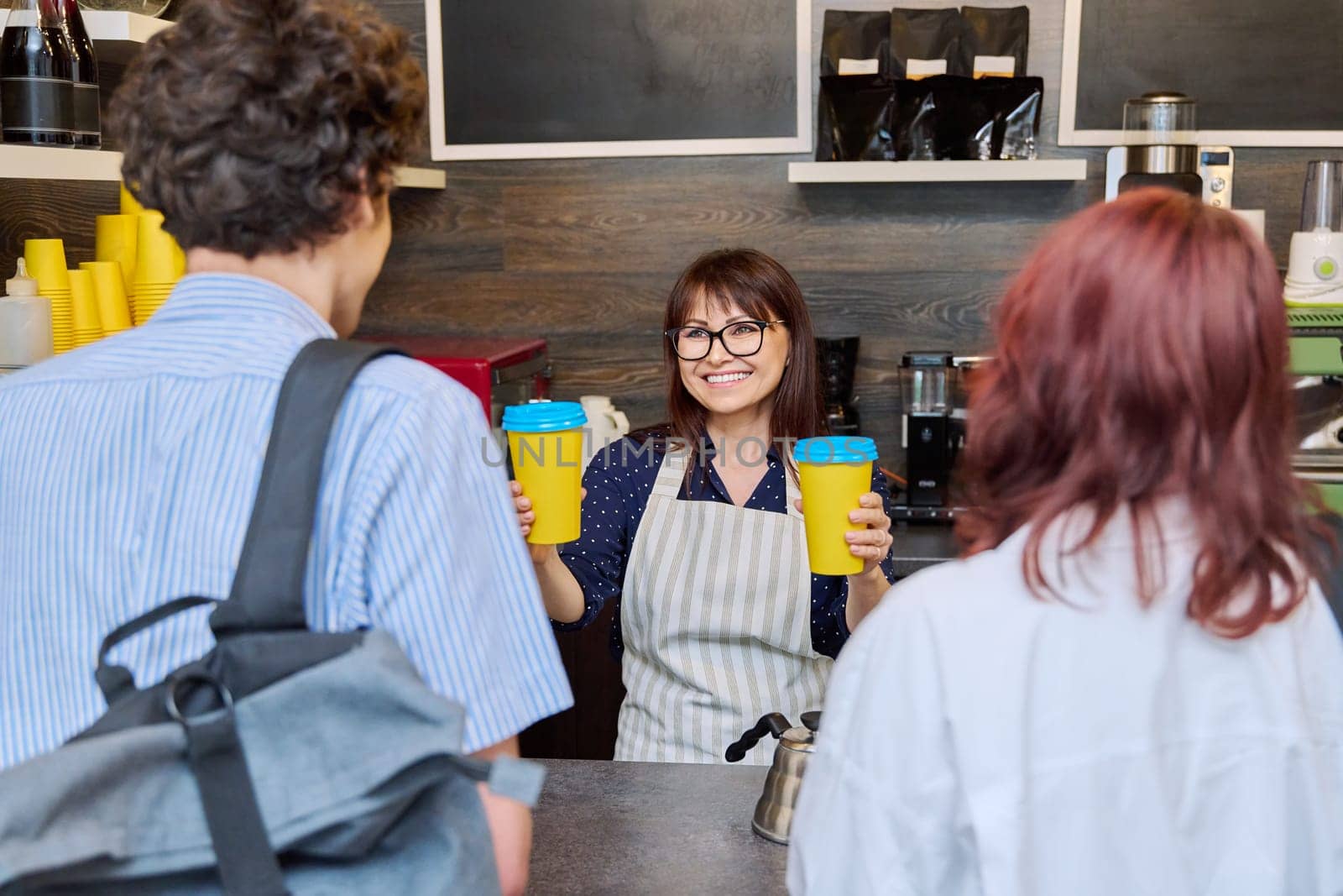 Female coffee shop worker serving couple of young customers giving paper cups of takeaway coffee. Food service occupation, small business, staff, job, work, people concept