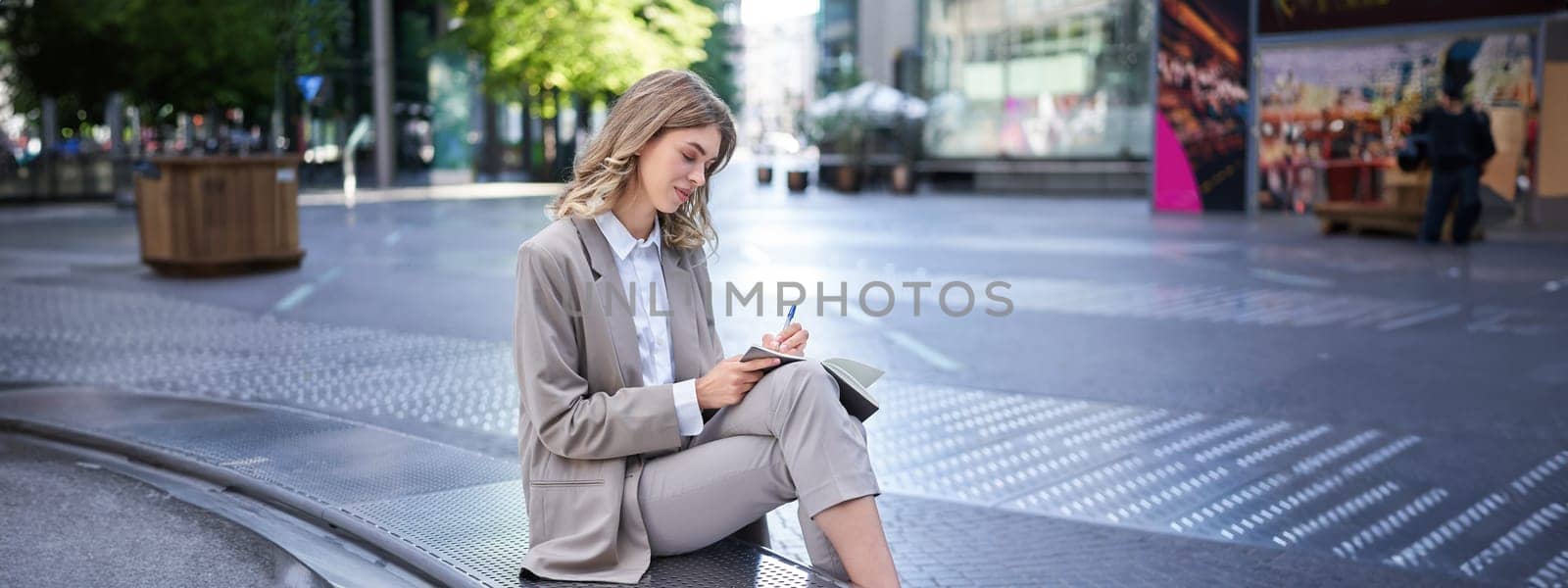 Businesswoman writing down her thoughts, corporate lady sits outdoors, works, brainstorming.