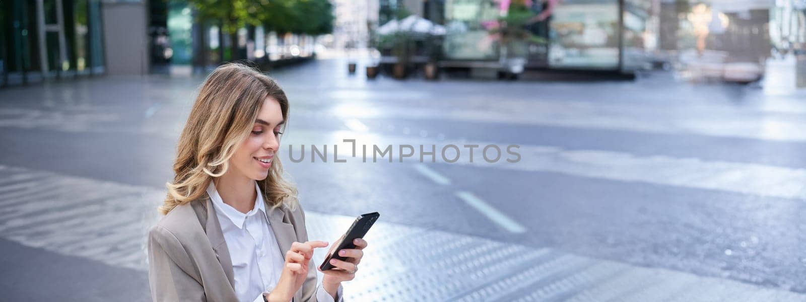 Vertical portrait of businesswoman in suit using her phone, relaxing outdoors, sitting on bench.