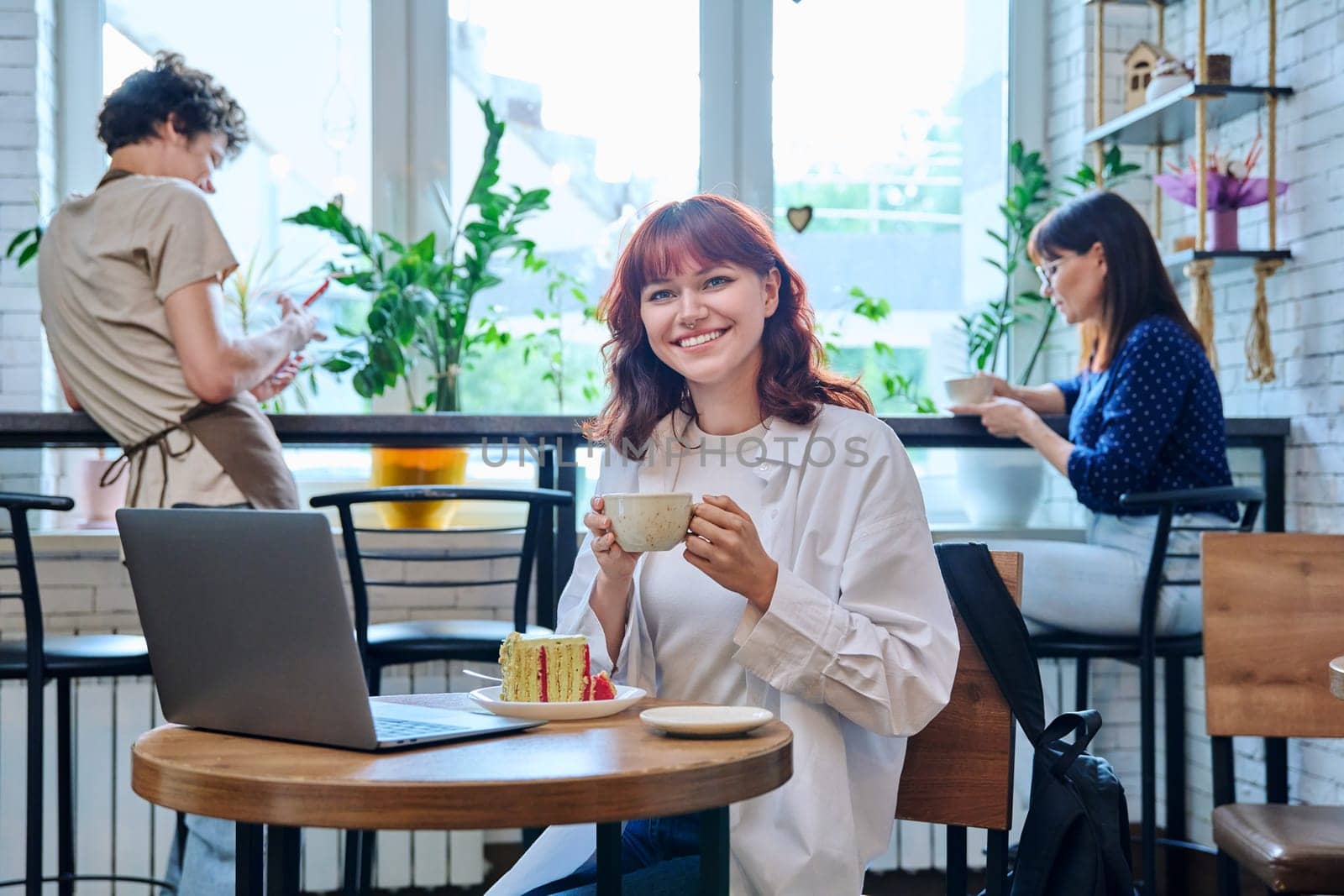 Female college student with laptop in cafe, with cup of coffee, piece of cake by VH-studio
