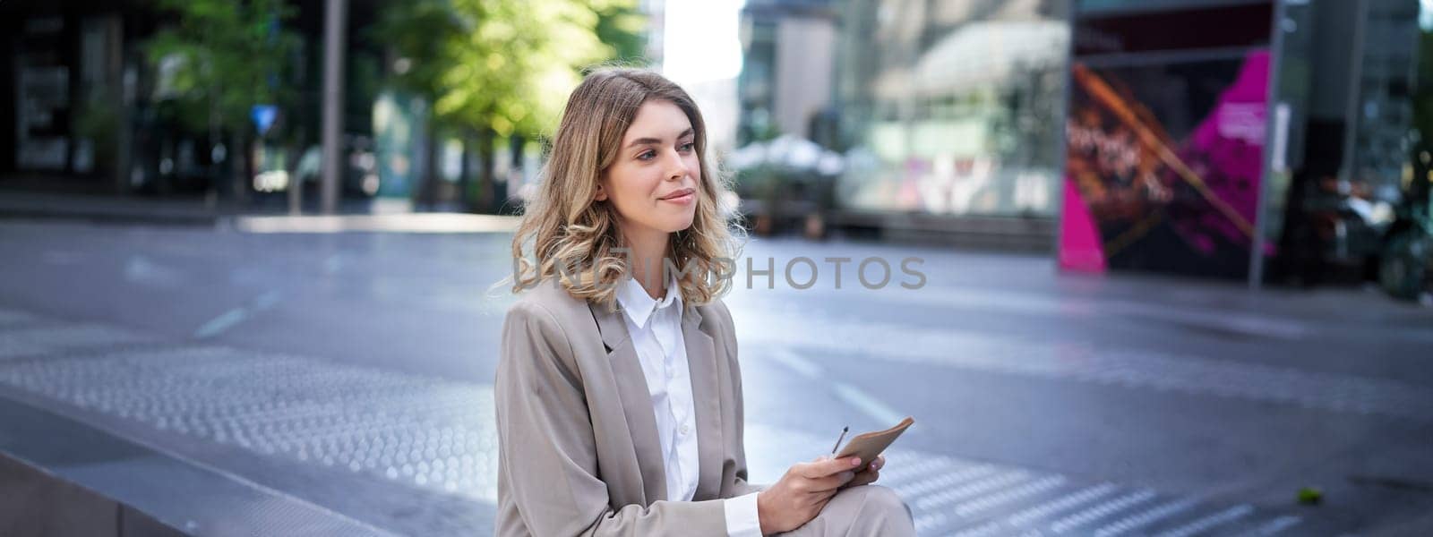 Young businesswoman preparing for speech, interview in company, writing down notes while sitting outside in city centre.