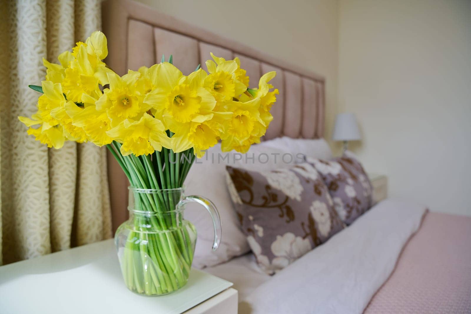 Bouquet of yellow flowers of spring daffodils in a vase on a bedside table in a bedroom interior