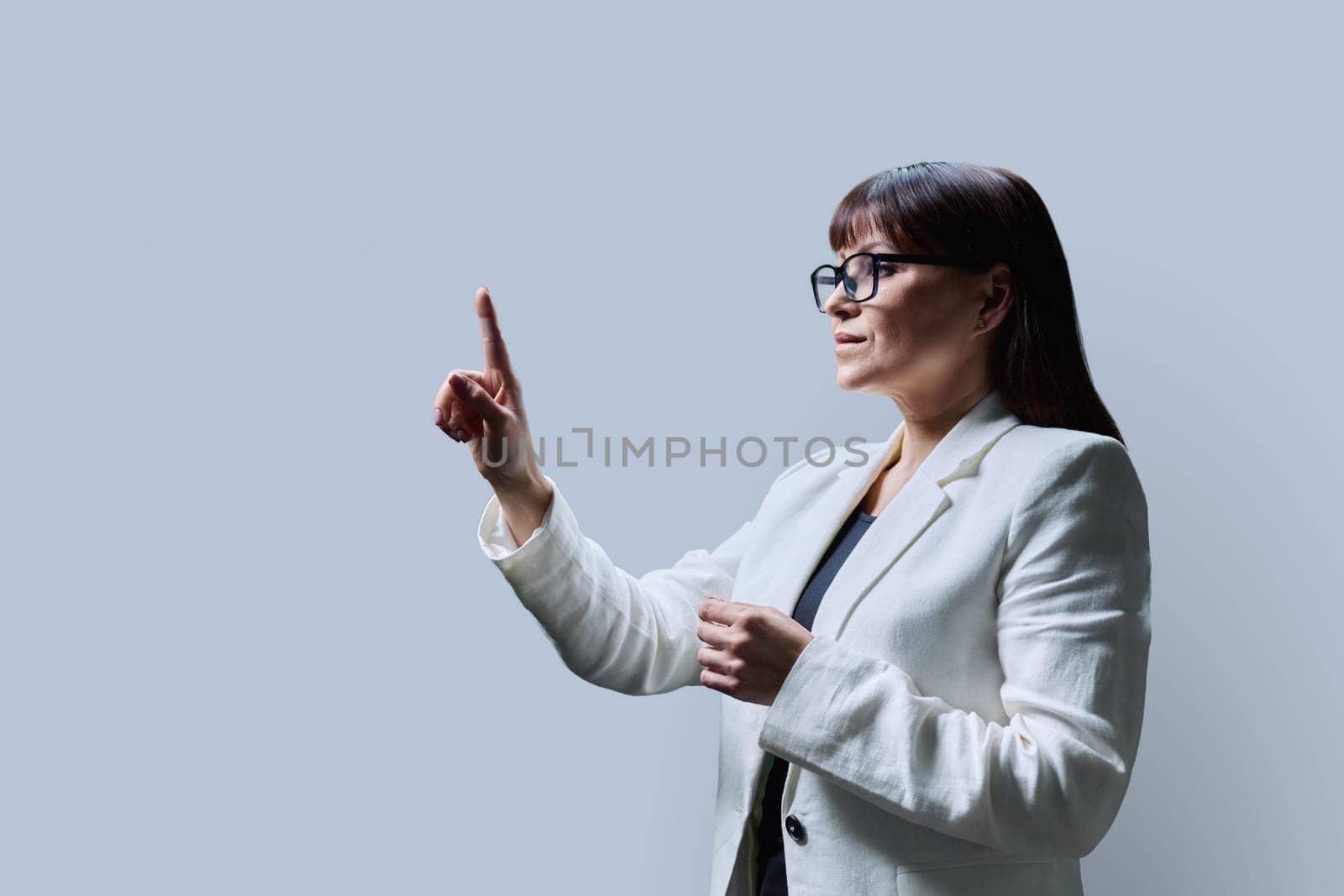 Mature business woman touching with finger on virtual screen, grey copy space background for your image text. Modern digital technology, business, finance, work, education, people concept