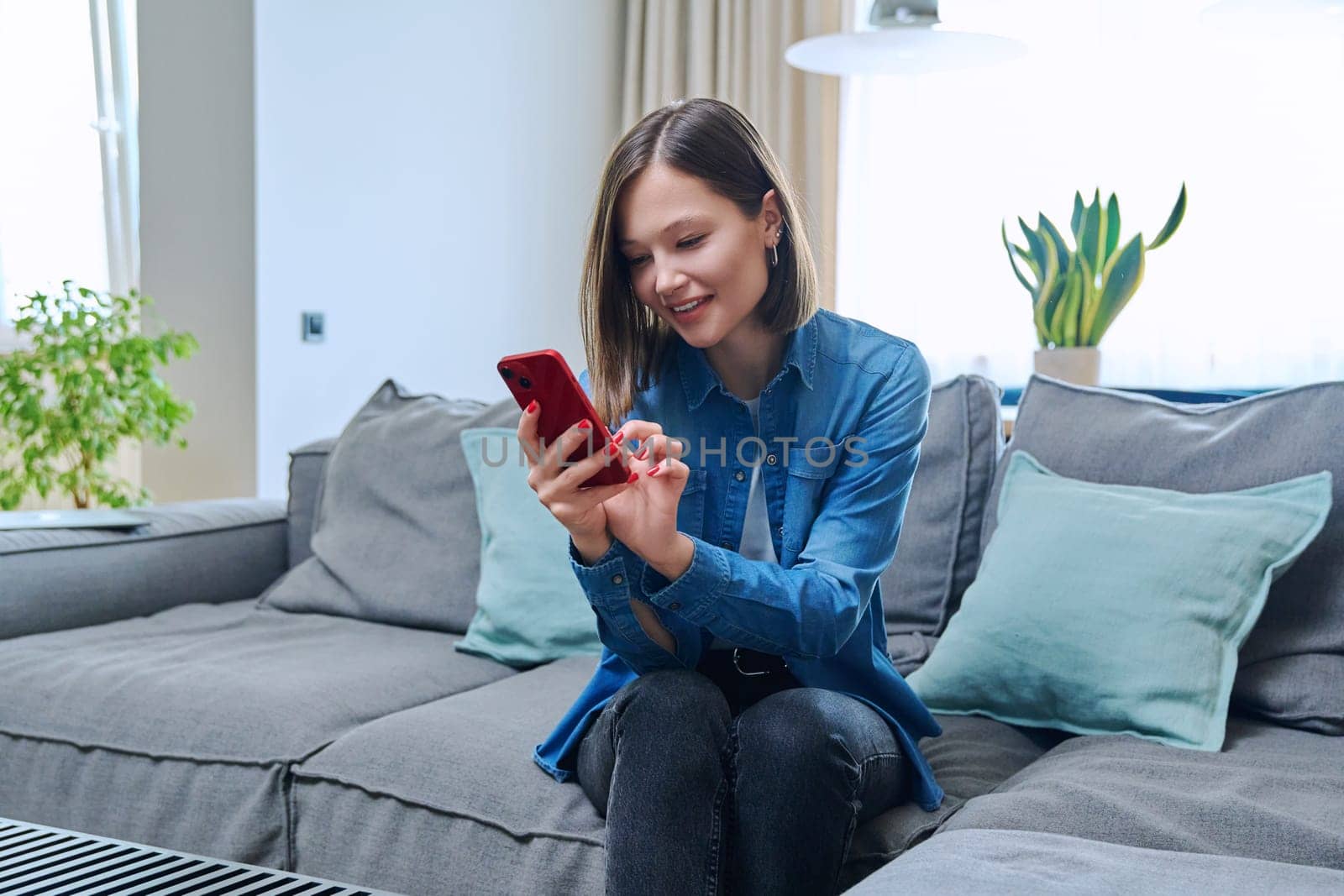 Young fashionable beautiful woman at home on couch in living room using smartphone. Internet online service, technology, mobile applications for study leisure life work shopping
