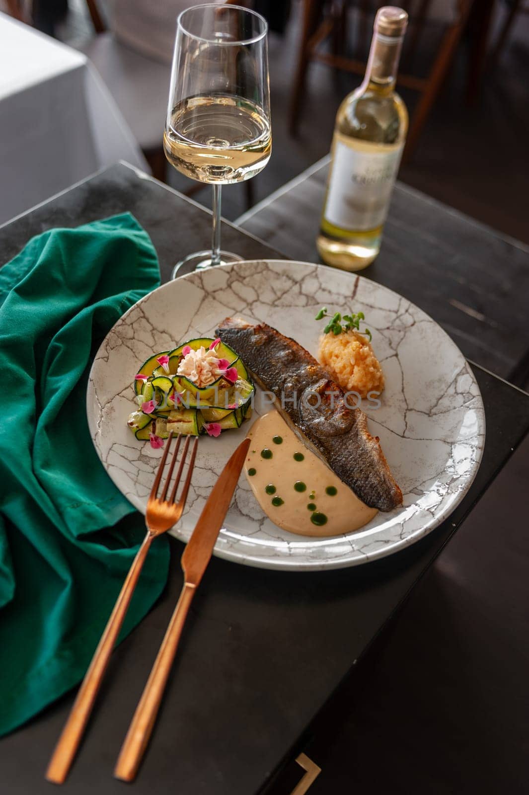 Sea bass or dorado fillet with baked zucchini and sauce on a gray plate in a restaurant