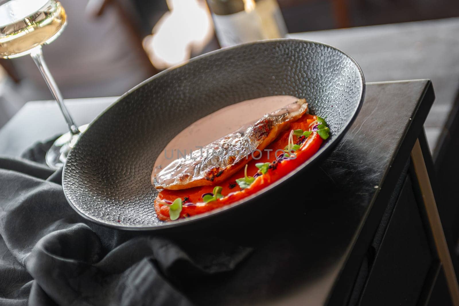 Sea bass or dorado fillet with sweet potato puree and flying fish roe sauce on a black plate in a restaurant