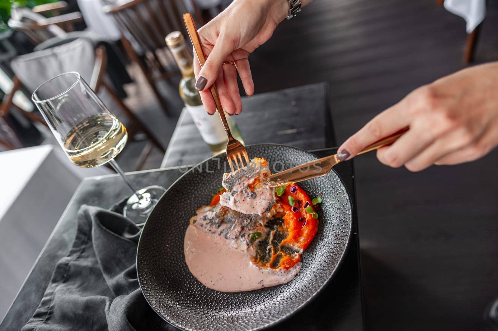 Sea bass or dorado fillet with sweet potato puree and flying fish roe sauce on a black plate in a restaurant