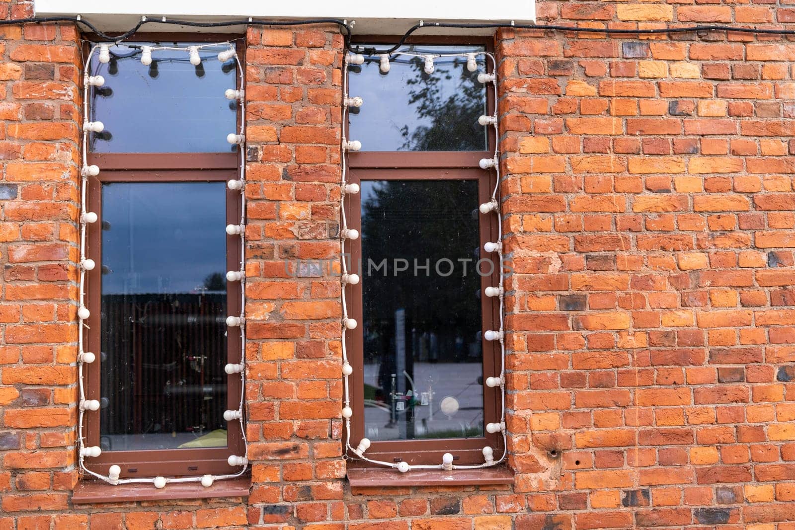 large windows in a red brick wall. Industrial design in the design of a city cafe or restaurant. Garlands of light bulbs around the windows.