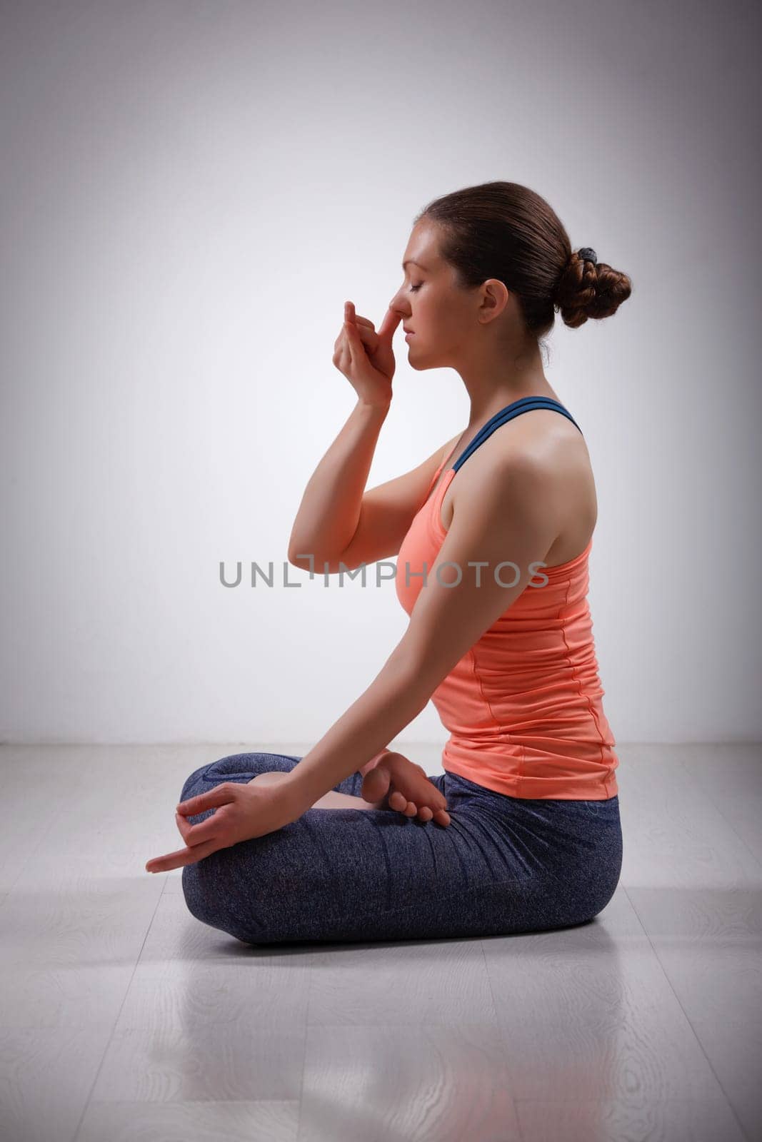 Beautiful sporty fit yogini woman practices pranayama breath control exercise in yoga asana Padmasana - lotus pose with Vishnu mudra in studio