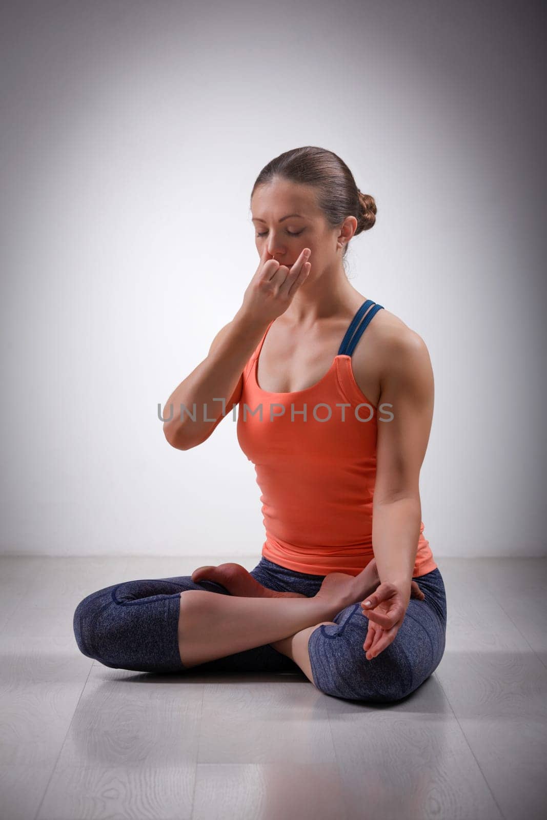 Beautiful sporty fit yogini woman practices pranayama breath control exercise in yoga asana Padmasana - lotus pose with Vishnu mudra in studio