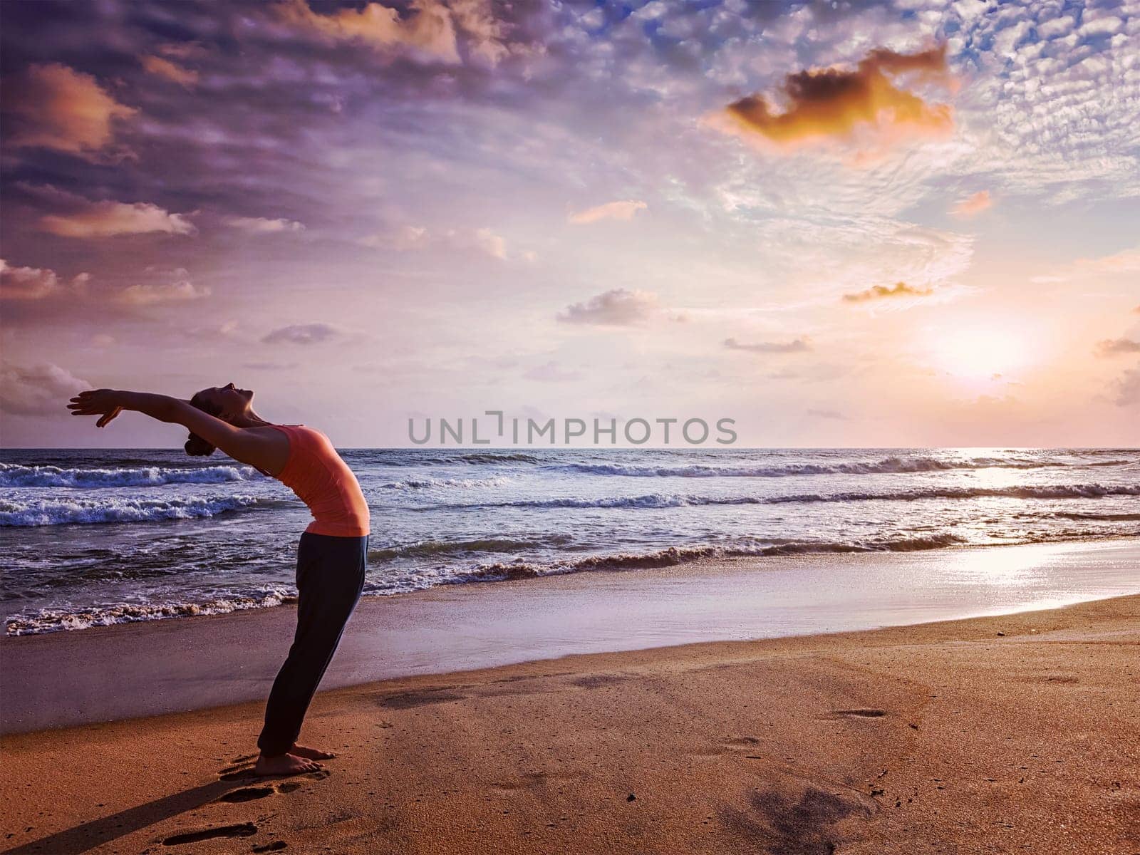 Vintage retro effect hipster style image of young sporty fit woman doing yoga Sun salutation Surya Namaskar pose Hasta Uttanasana on tropical beach on sunset