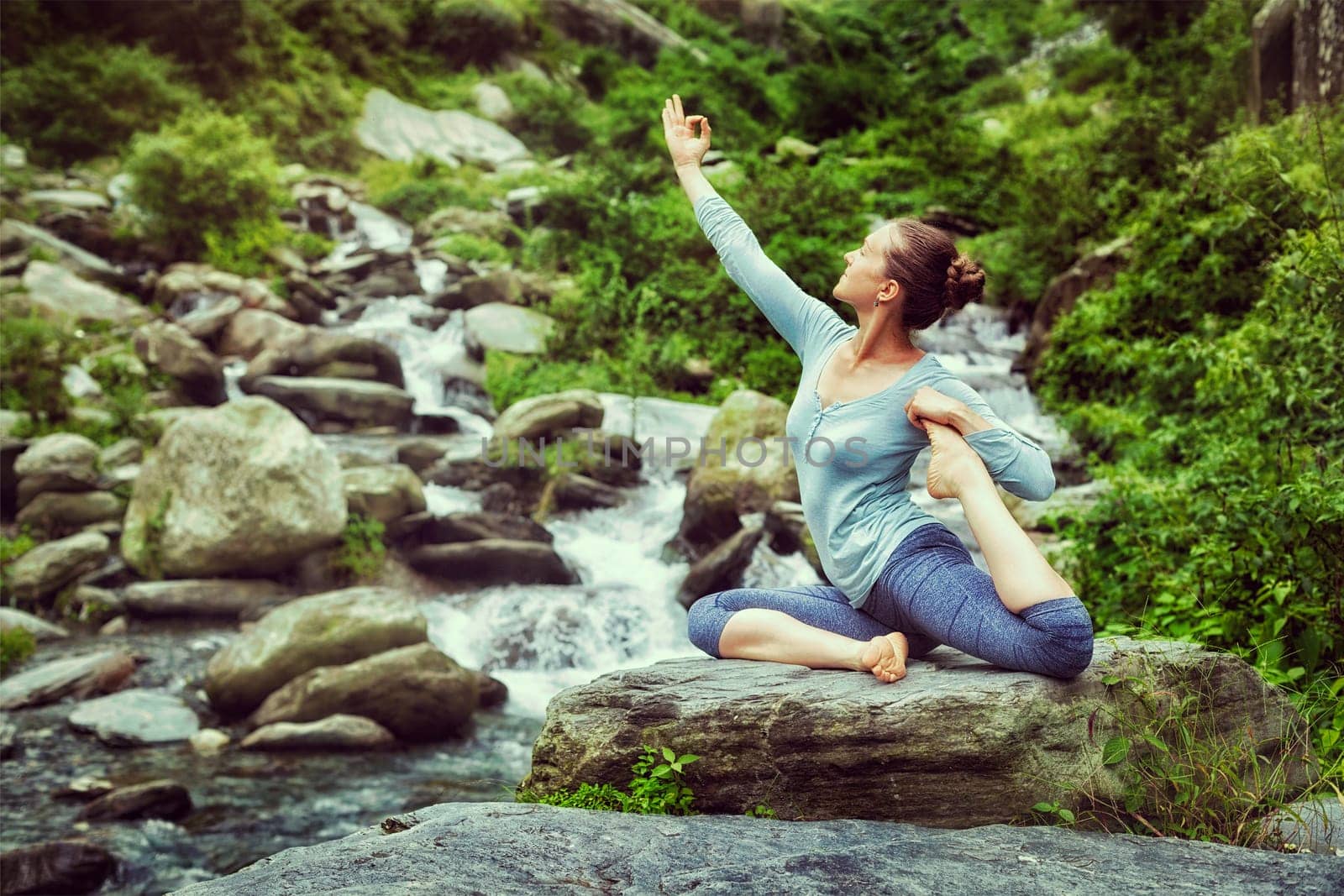 Vintage retro effect hipster style image of sporty fit woman doing yoga asana Eka pada rajakapotasana - one-legged king pigeon pose at tropical waterfall