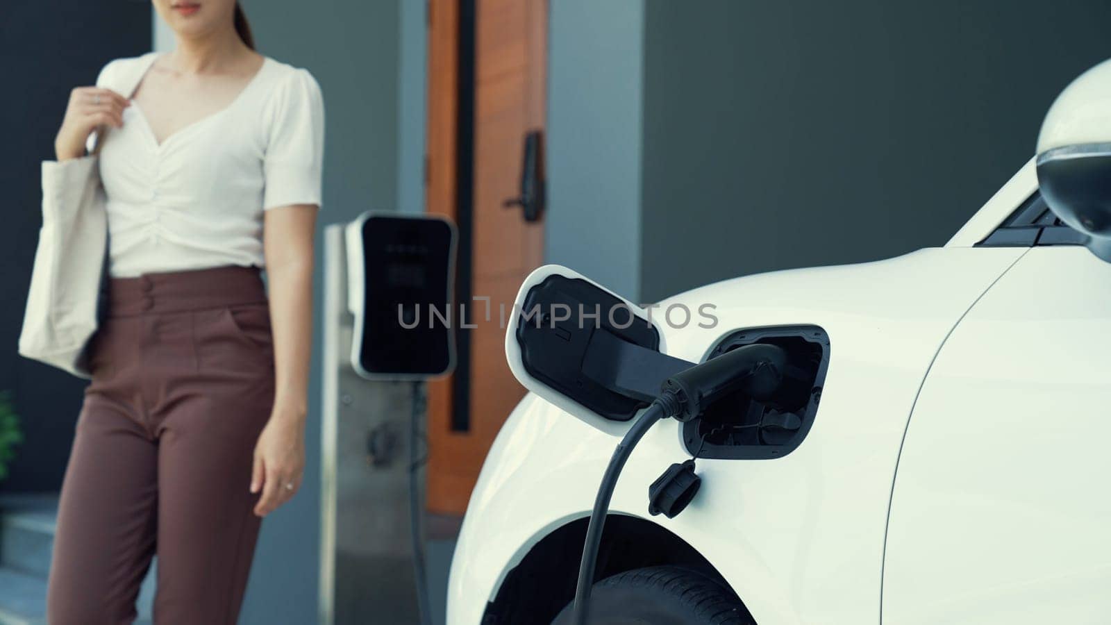 A woman unplugs the electric vehicle's charger at his residence. Concept of the use of electric vehicles in a progressive lifestyle contributes to a clean and healthy environment.