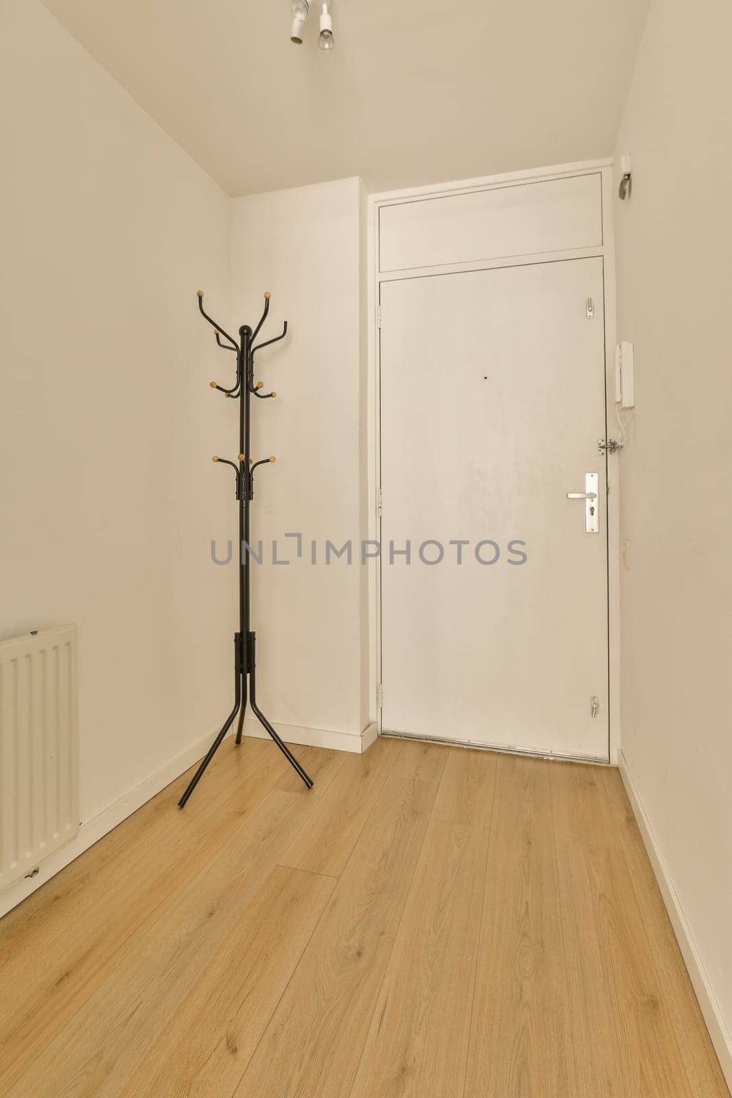 an empty room with wood floors and white walls, including a black coat rack on the door to the left