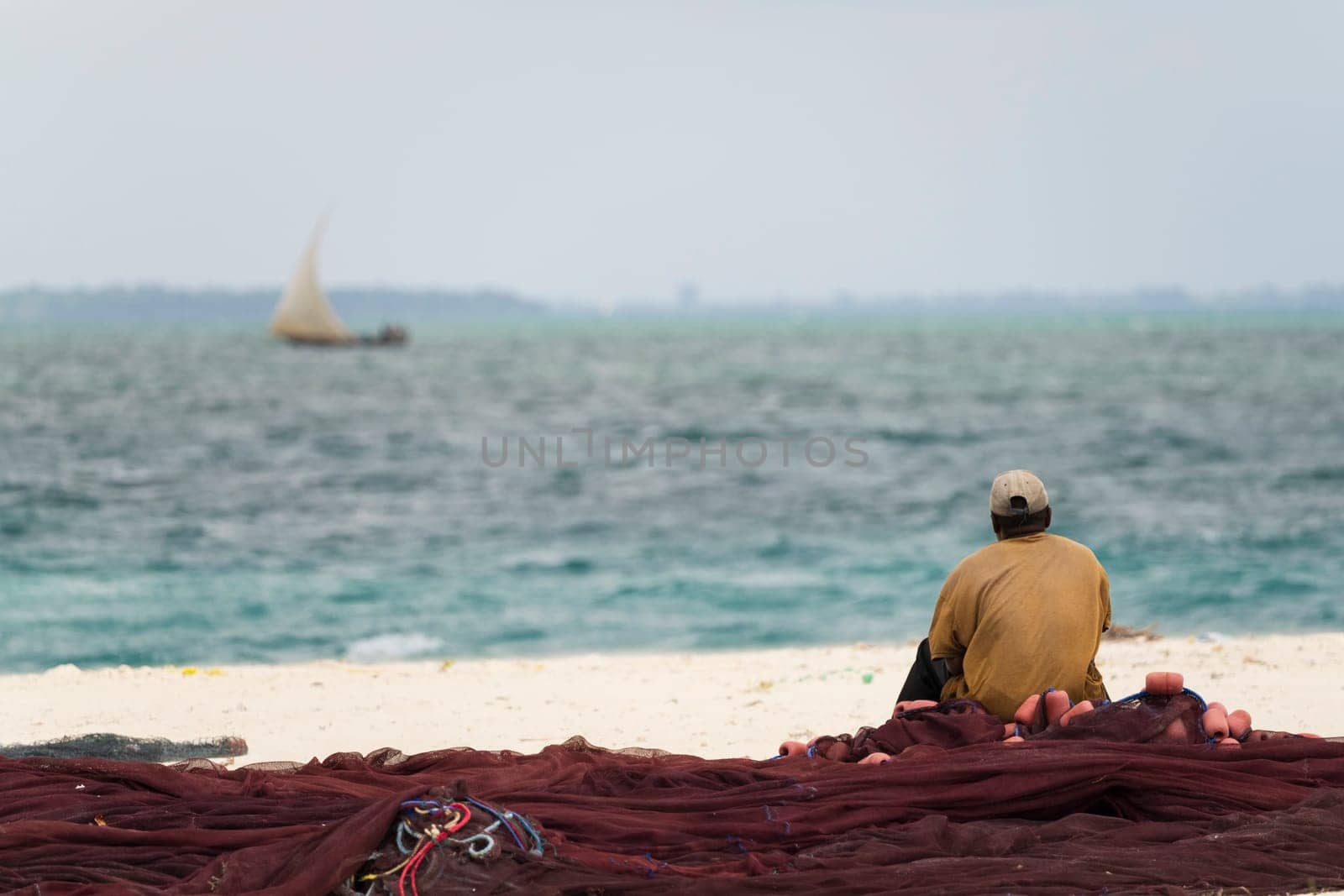 African fisherman sitting on fishing nets looks out to sea by Robertobinetti70