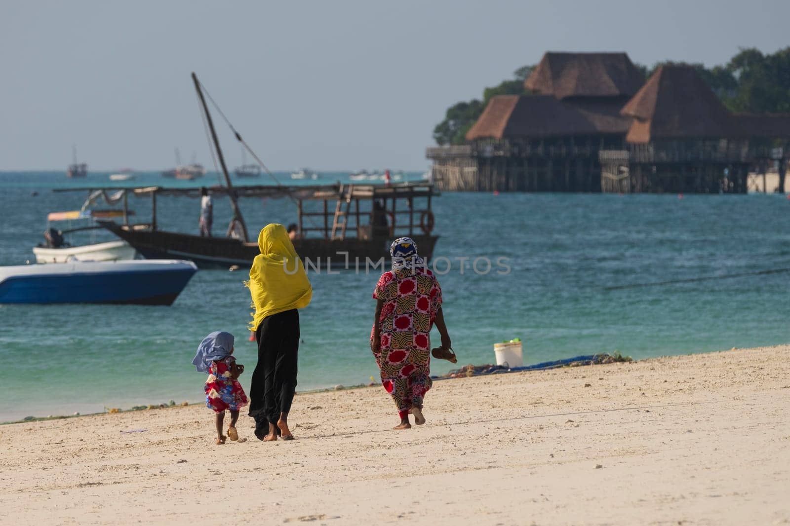 Two African women and a little girl walk along the sandy beach by Robertobinetti70