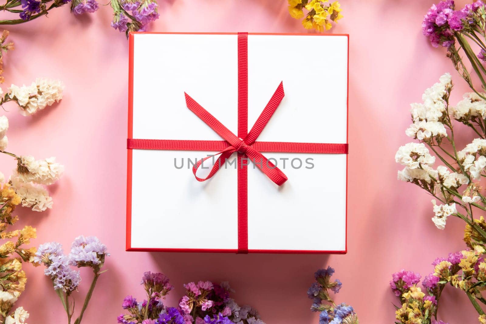 Background with colorful floral frame and gift box with red beautiful ribbon.