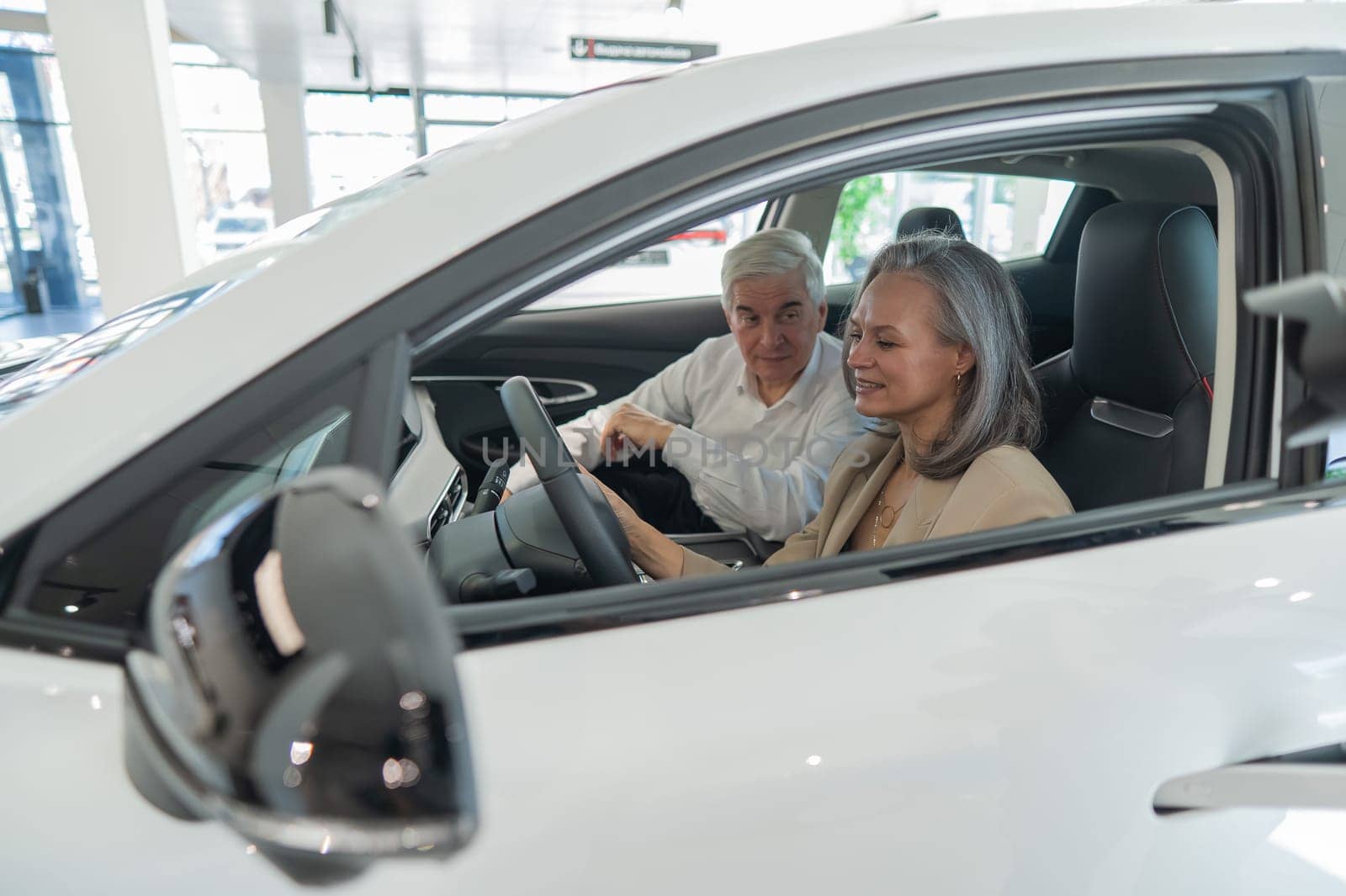 An elderly couple chooses a new car at a car dealership. Mature woman driving