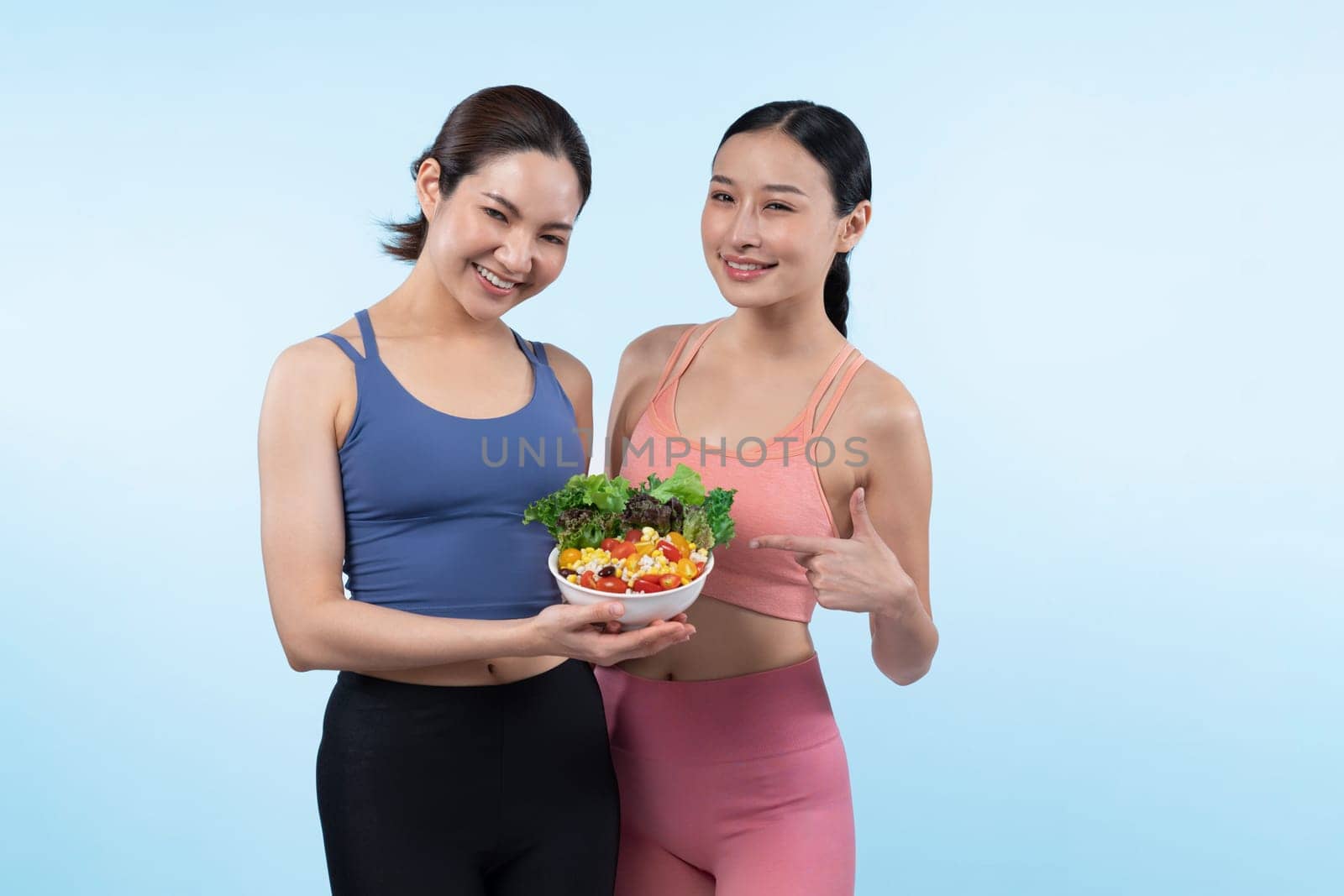 Asian woman in sportswear holding salad bowl on isolated background. Vigorous by biancoblue