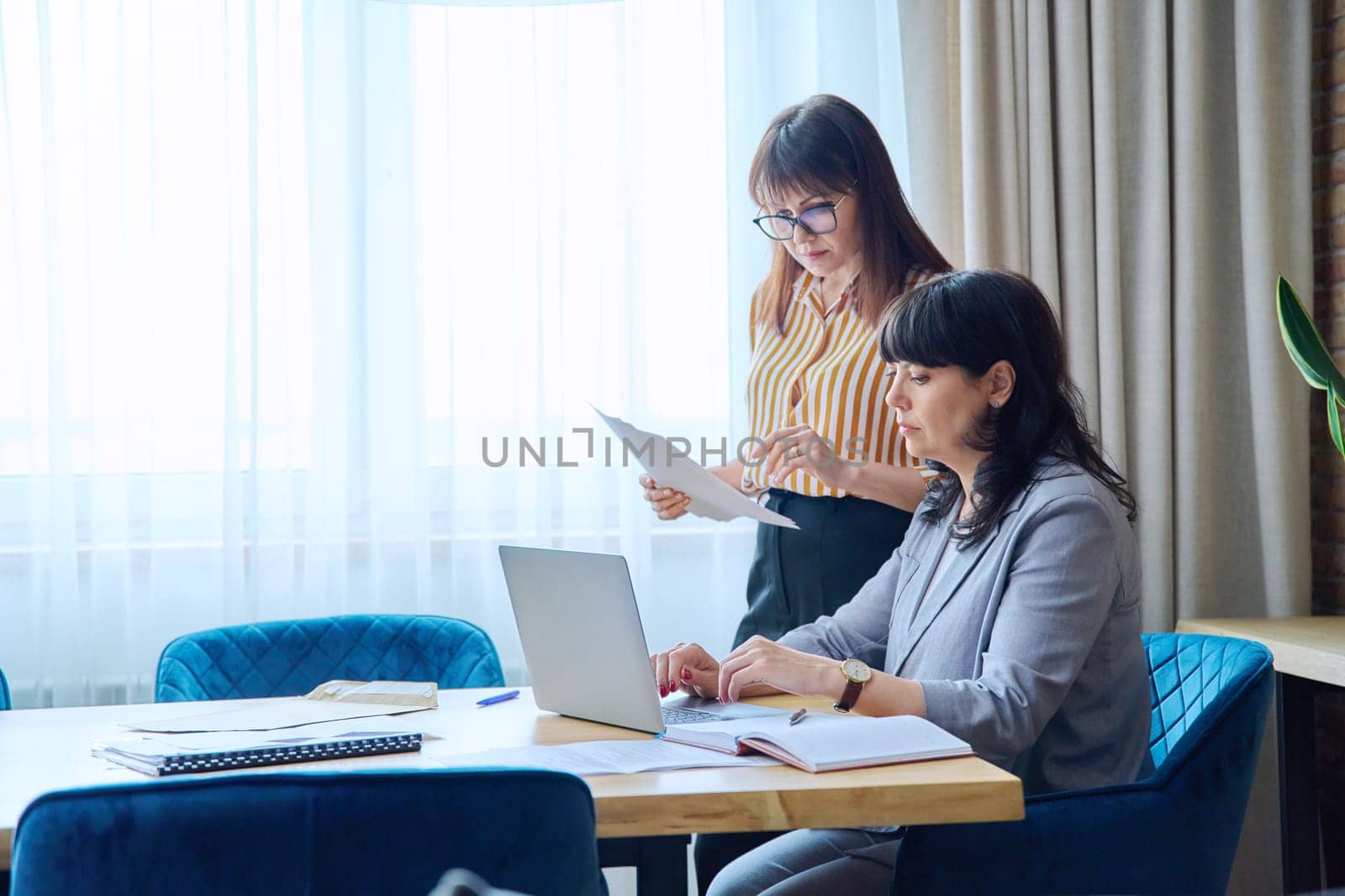 Two mature business women colleagues employees working together in office, middle-aged females preparing contract financial legal plan. Work professionals teamwork communication 40s 50s people on job