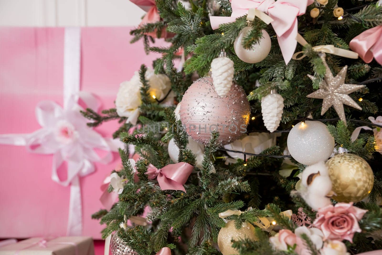 Giftboxes, pink and white christmas decorations balls hanging on a decorative white christmas tree.