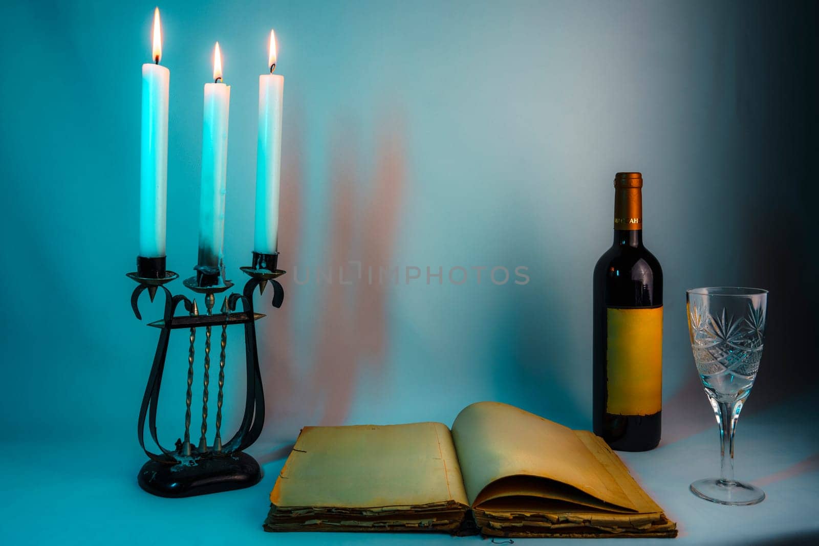 An open vintage book with yellowed pages, an antique candelabrum with burning blue candles, a wine bottle, and a glass, set in dim lighting, creating a mysterious and elegant atmosphere
