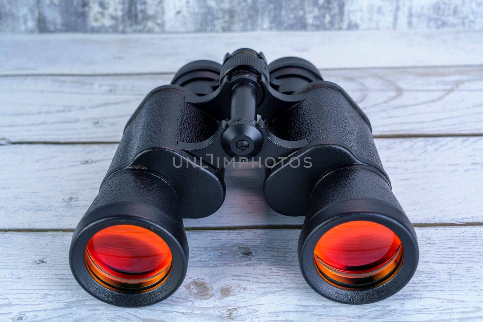 Close-up of black binoculars with red-tinted lenses placed on a white wooden surface, symbolizing exploration, vision, and outdoor adventure.