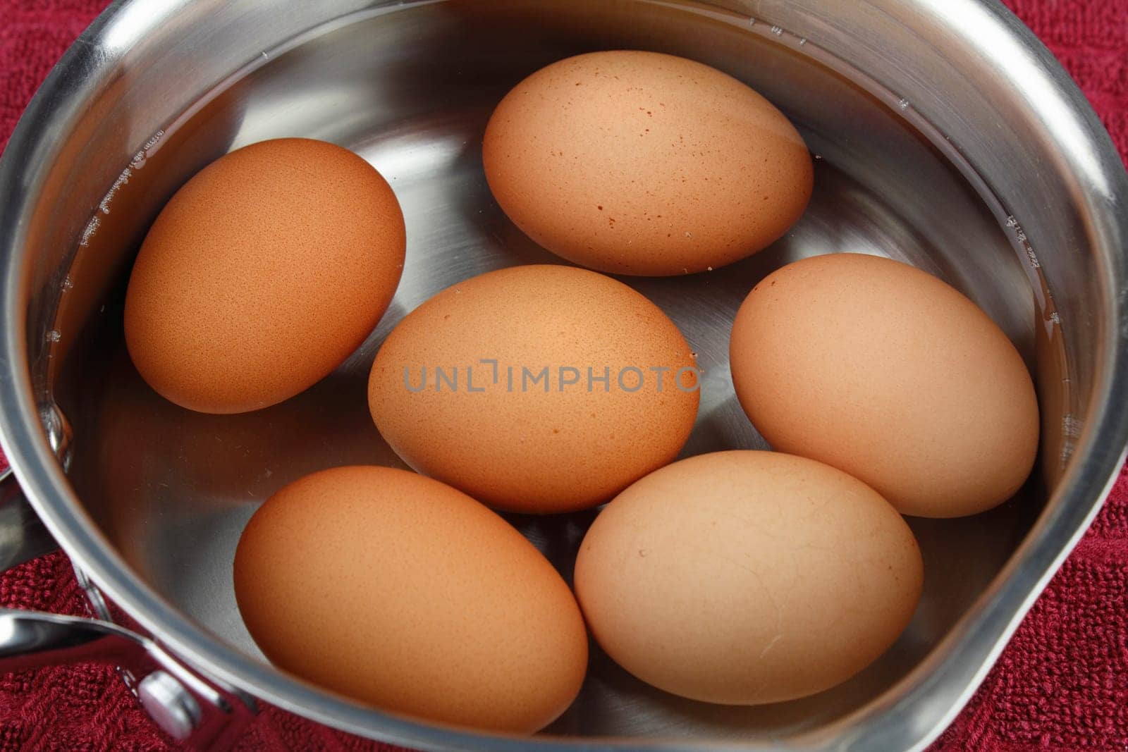 Six organic brown eggs in shell sit cooling in a pan of water after boiling.