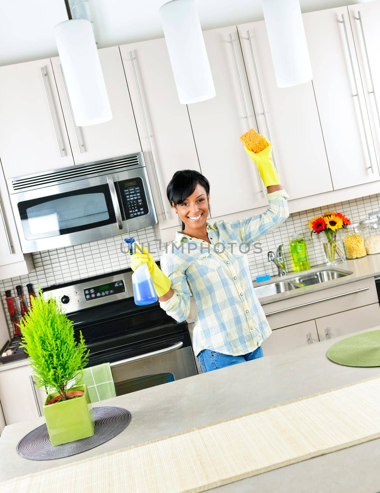 Smiling young black woman with sponge and rubber gloves cleaning kitchen