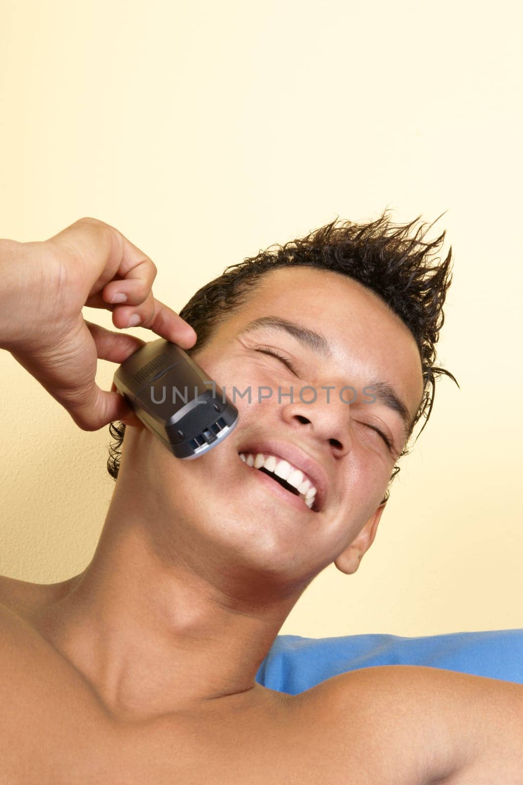Smiling young brazilian man holding a cordless phone, over a light yellow background, with copyspace.