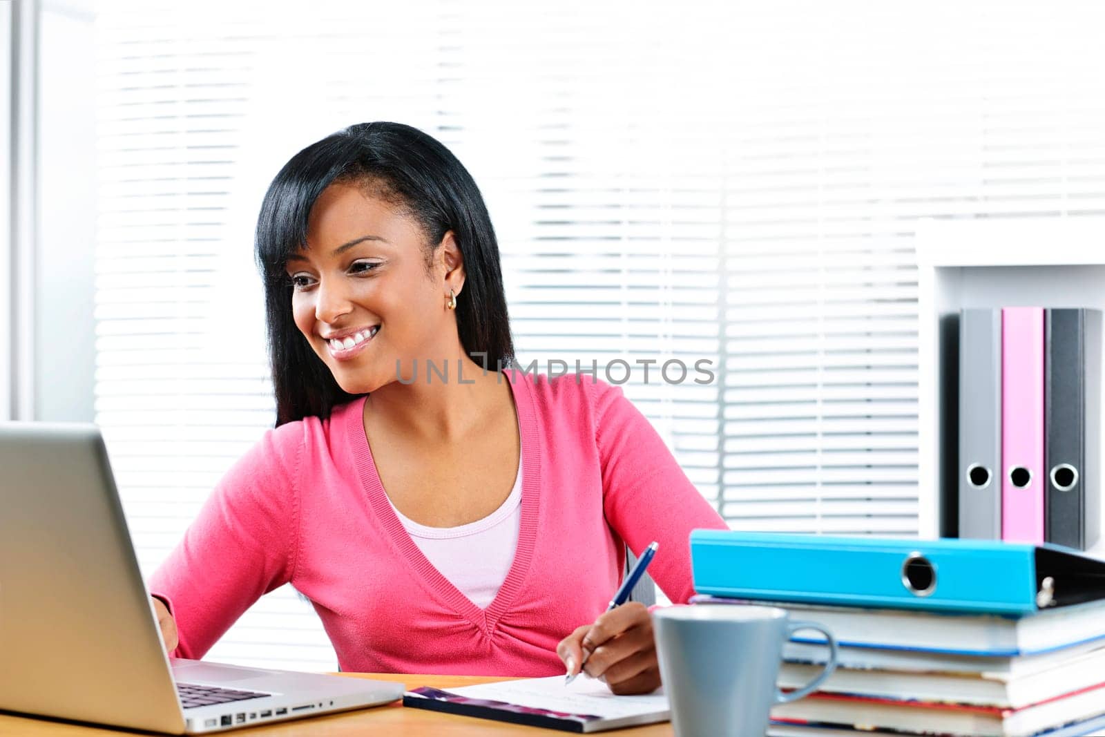 Smiling young black female student with computer and textbooks at desk