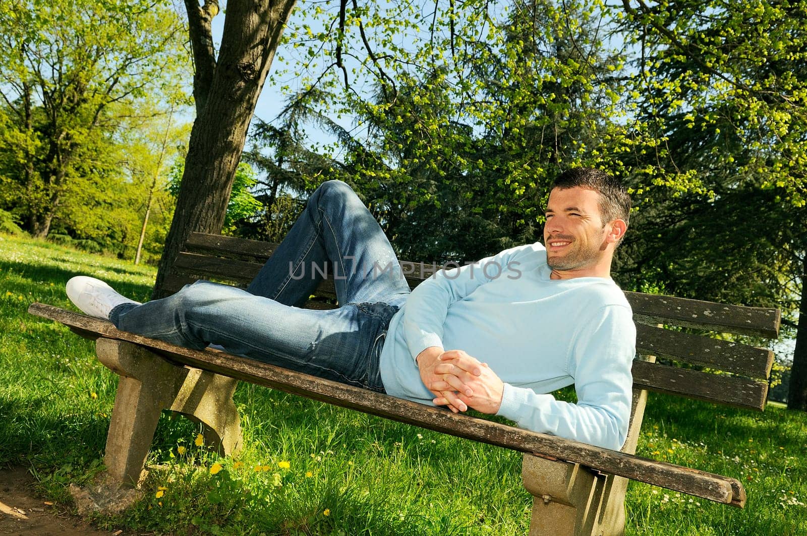 attractive man is relaxing on a bench in a natural environement