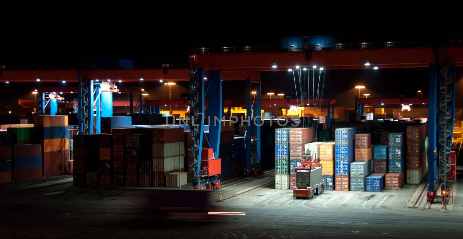 Busy Commercial Container port at night with cranes and cars moving containers