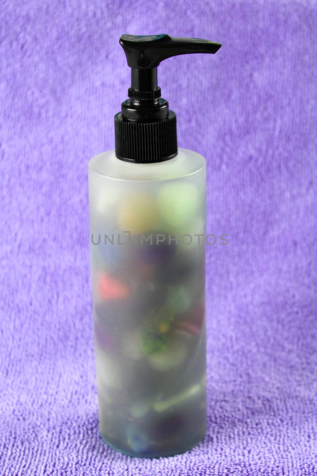 A transparent jojoba massage oil pump bottle is seen upright with various colored stones inside.