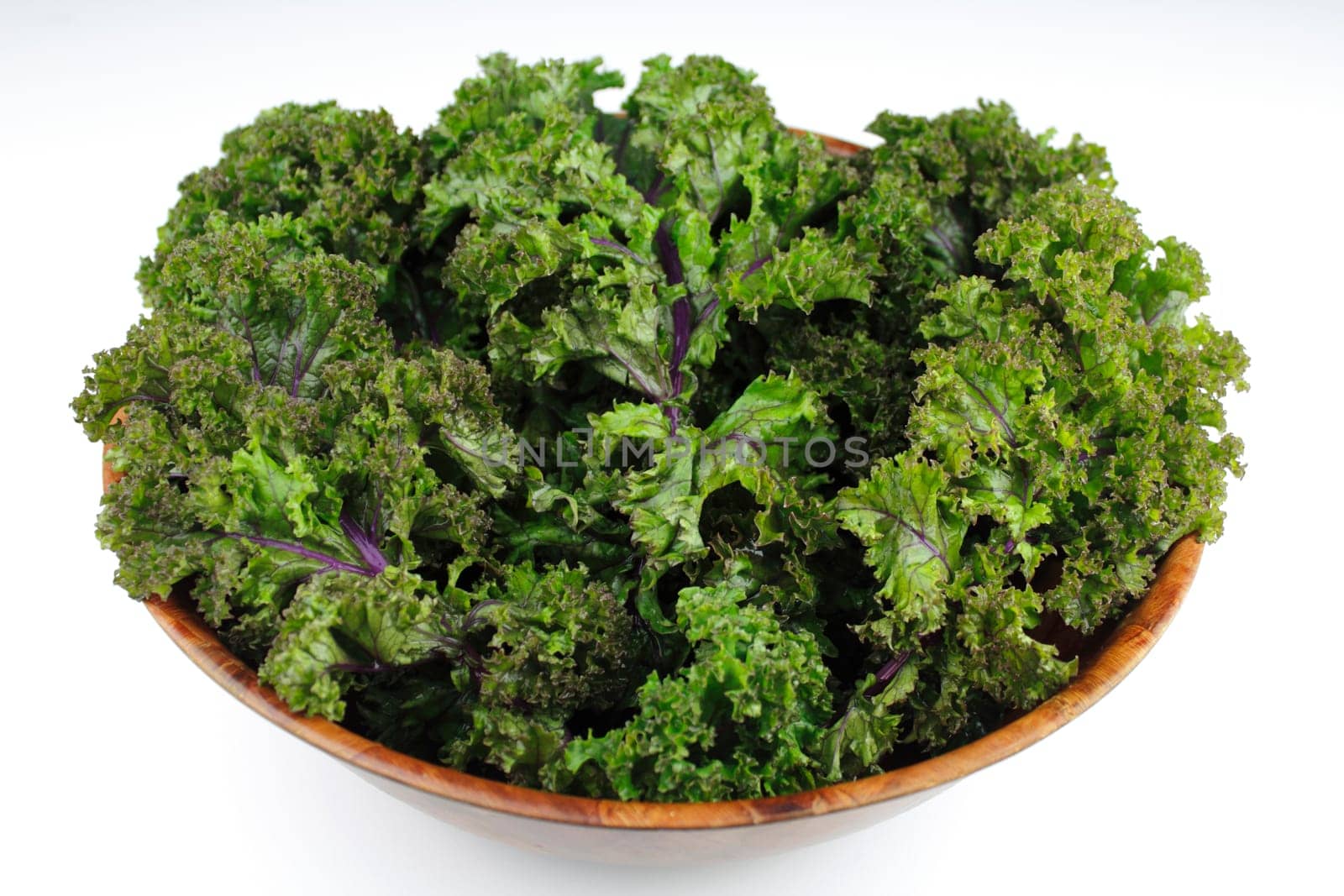 Wood bowl of red kale, green leaf with purple veins, on a white background.