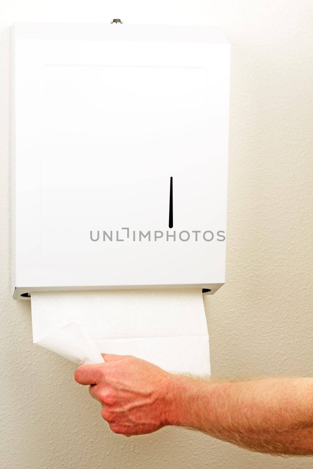 A hand is pulling down and out a white folded sheet of disposable paper to dry hands from a wall box.