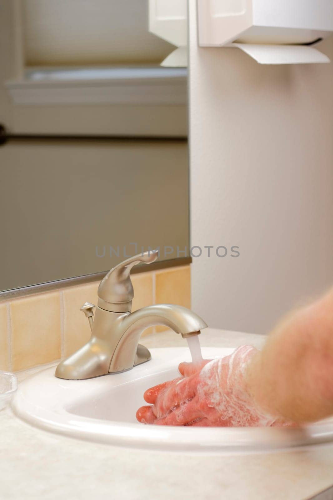Male hands cleaning skin with white soap lather at a sink.