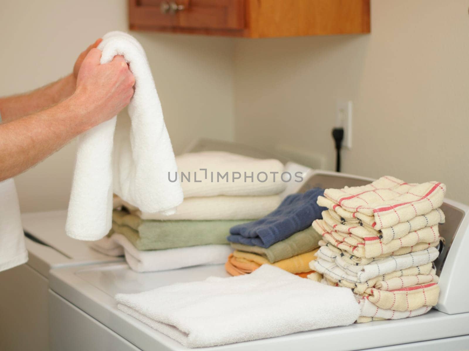 Arms and hands of a male folding towels onto a dryer and washer in a laundry room.