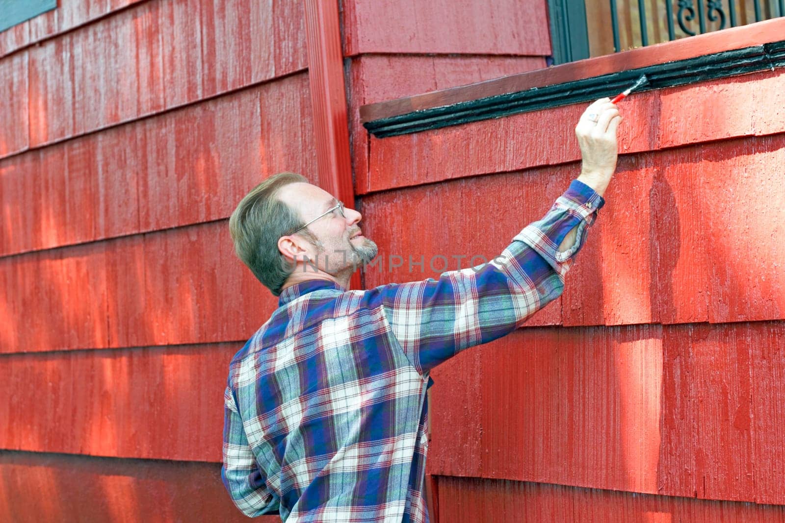 Man in his 40s adding paint detail to the side of a front porch.