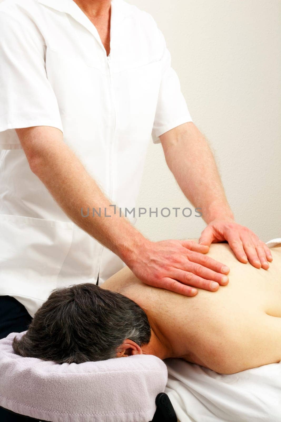 Male laying face down getting an upper torso massage from a professional male massage therapist.