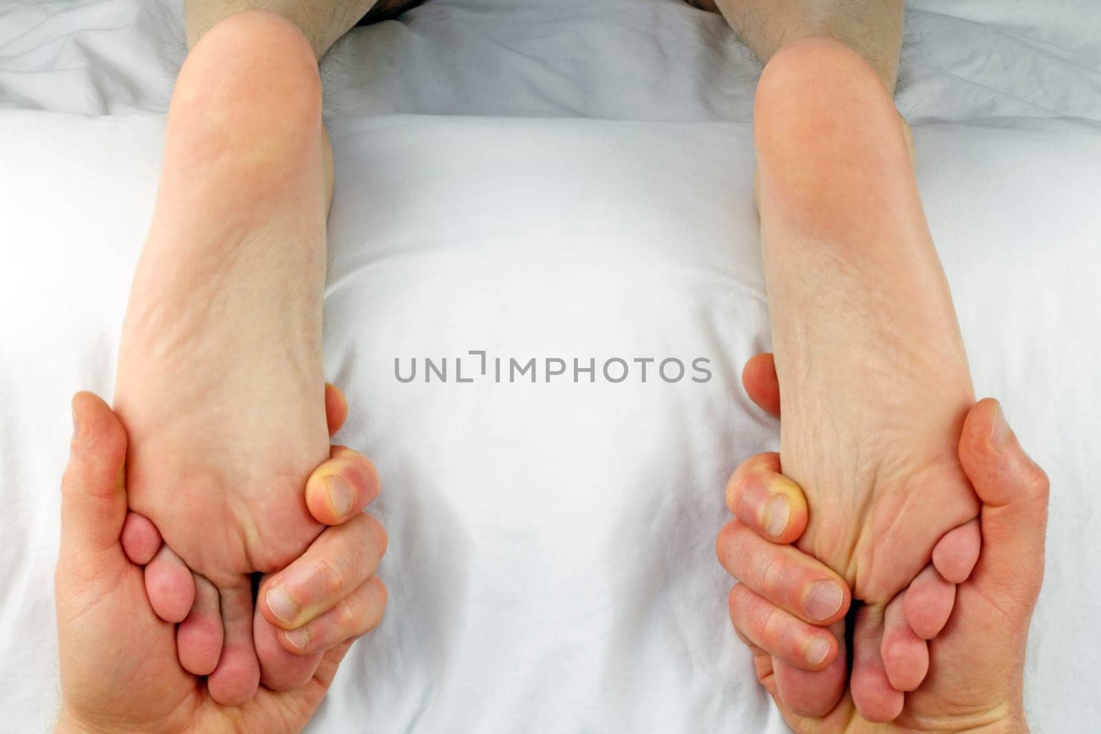 Male getting both feet massaged with reflexology at the same time by the hands of a male massage therapist.