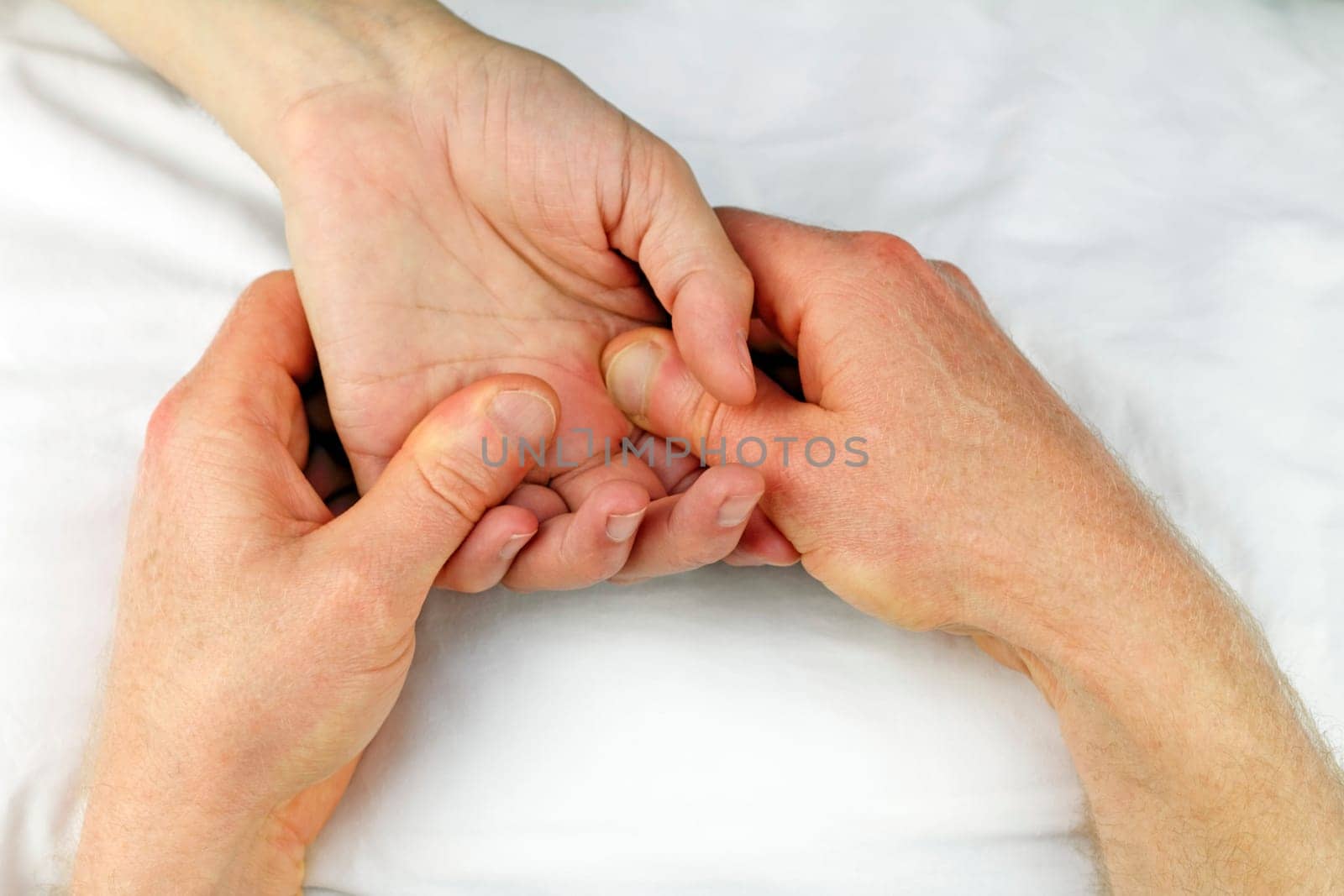 Male hand being massaged below fingers with two hands by a massage therapist.