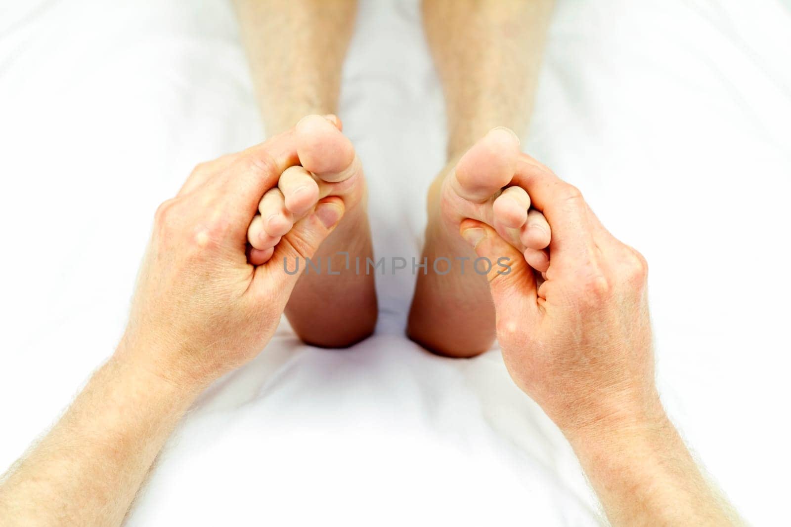 Male massage therapist hands giving a reflexology treatment to the soles of each foot of a patient.