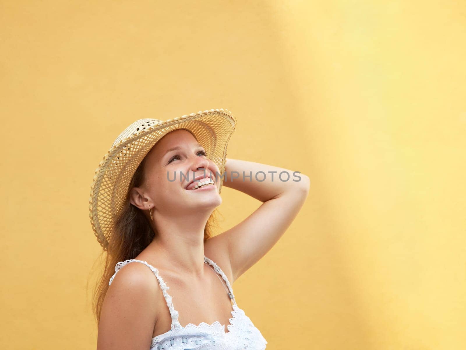 young adult blonde woman in straw hat laughing against yellow wall. Horizontal shape, side view, copy space