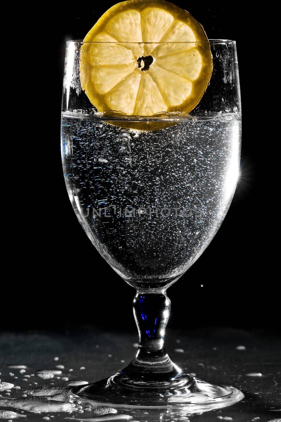 Slice of lemon drops into a glass of water and splashes