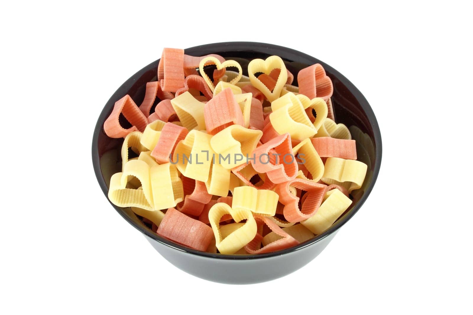 Raw colored pasta in form of heart in black bowl isolated on white background