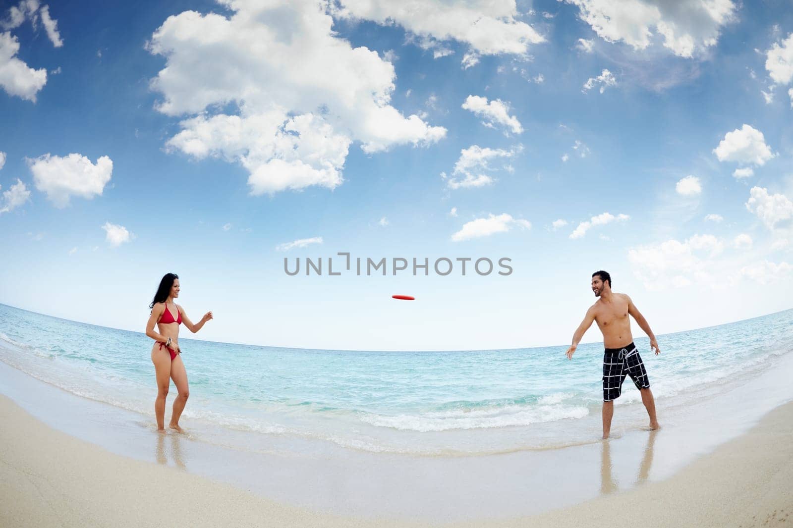 boyfriend and girlfriend playing with frisby on tropical beach. Horizontal shape, full length, fisheye