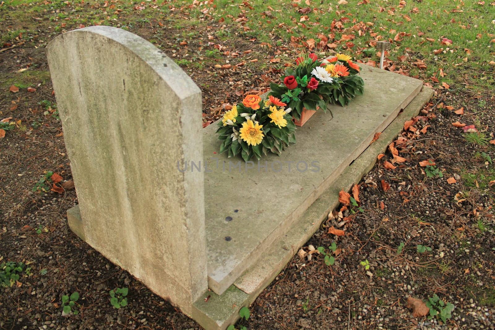 Tomb covered with colored flowers with autumn colored red leaves in a cemetery