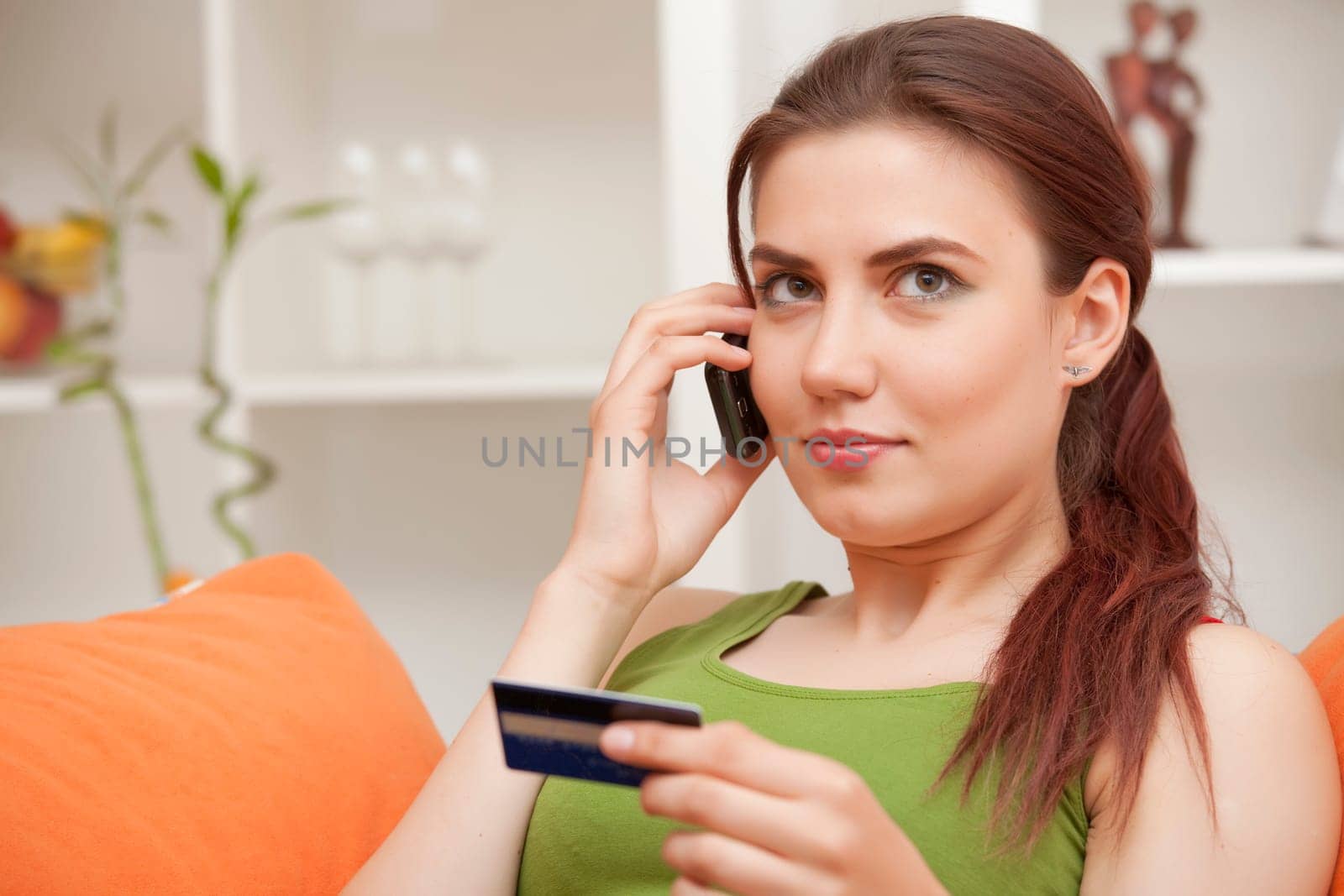 young woman holding credit card and making purchase on cell phone